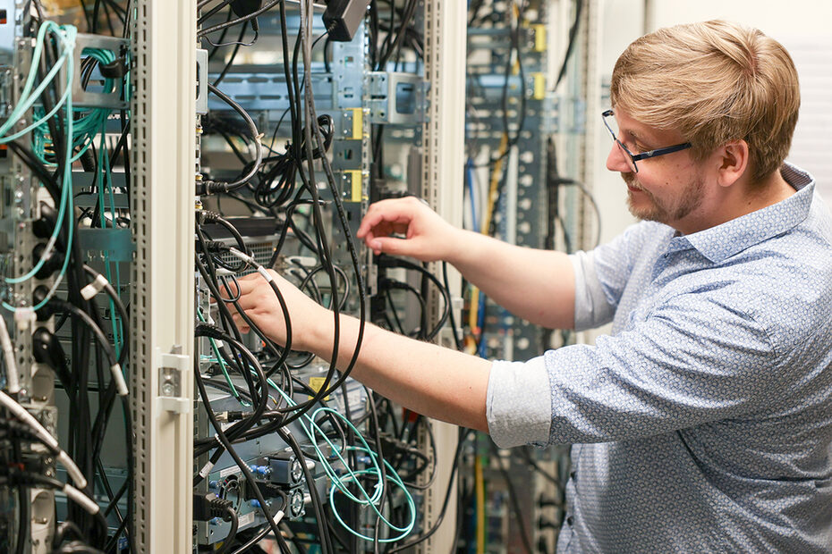 Ein Mann vor einem Serverschrank mit Kabeln, die er kontrolliert.